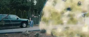 A man in a driveway reaches toward a large, yellow force-field